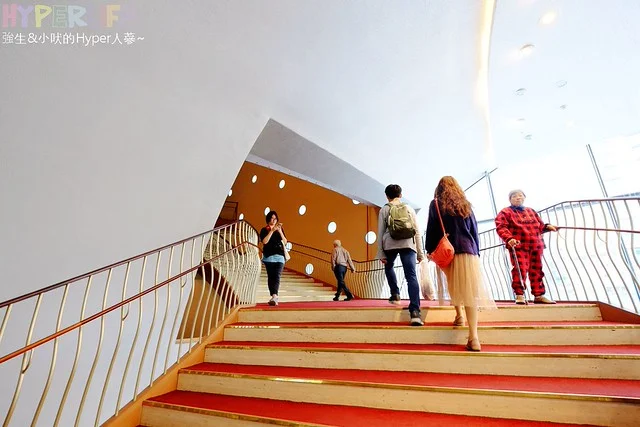 Nhóm người bước trên cầu thang hiện đại, phong cách tóc ivy league nam gọn gàng giữa không gian kiến trúc cam trắng