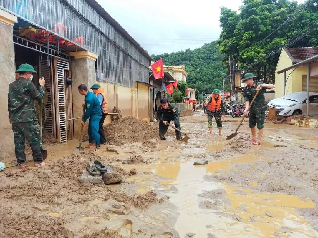 Bộ đội và người dân dọn bùn đất sau lũ lụt trên đường làng