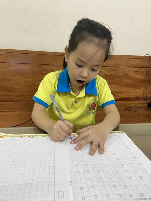 hình ảnh học tập của một bé gái đang tập viết chữ trong vở