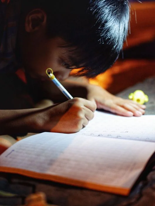 Hình ảnh học tập của một em bé đang chăm chú viết bài trong không gian tối.